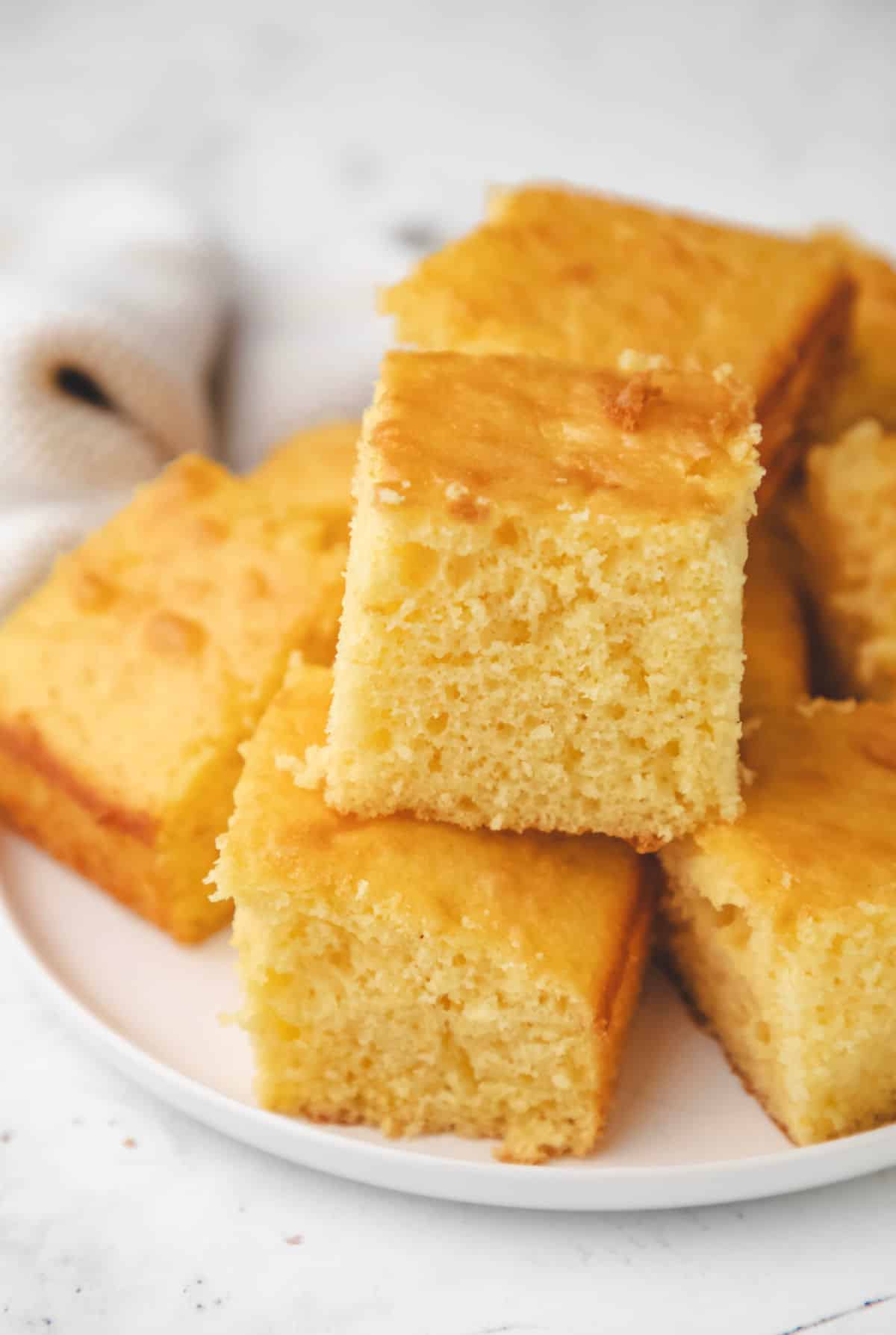 A plate full of stacked pieces of sweet cornbread. 