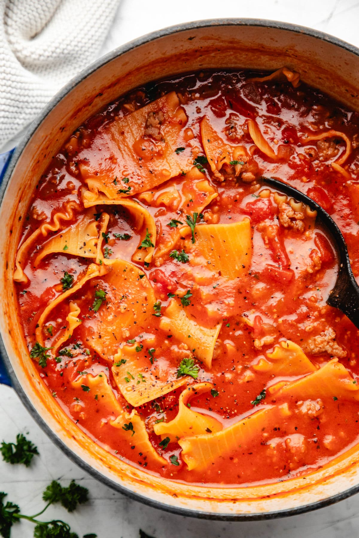 A black spoon in a pot of lasagna soup. 