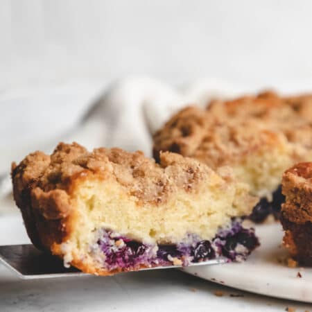 A cake server holding a slice of blueberry coffee cake.