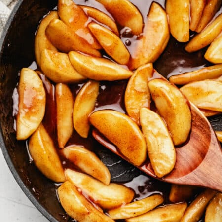 A wooden spoon scooping up cinnamon apples in a cast iron skillet.