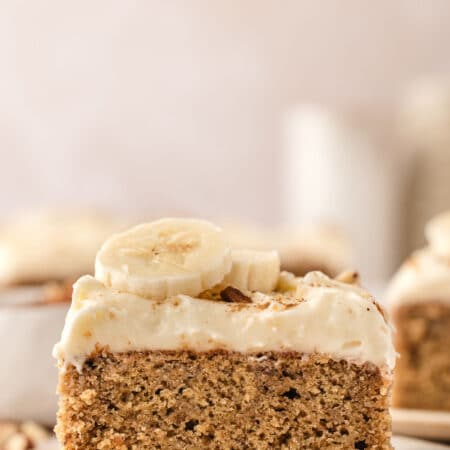 A slice of banana cake topped with cream cheese frosting and slices of fresh banana.