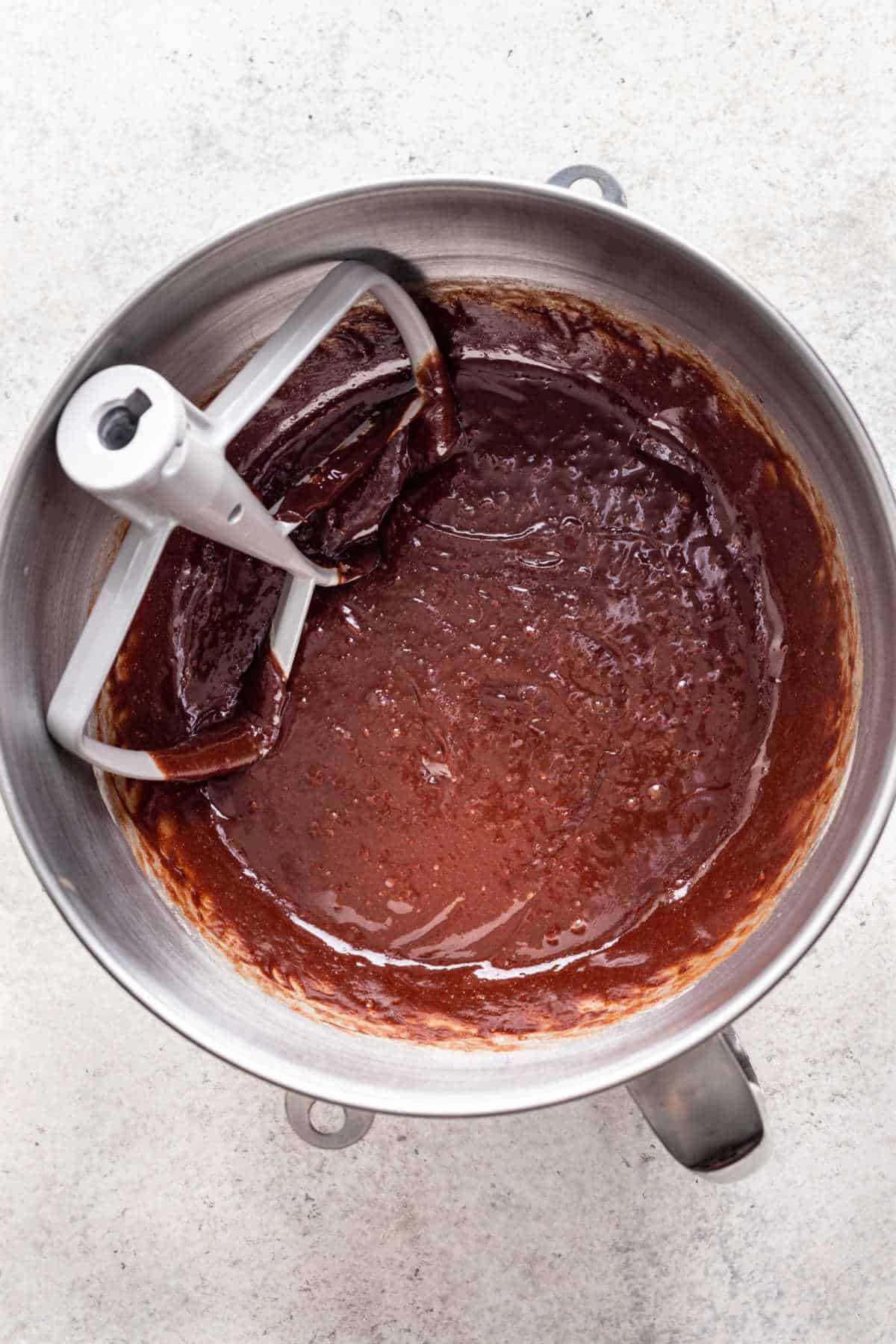Melted chocolate mixed into egg mixture in a silver mixing bowl. 