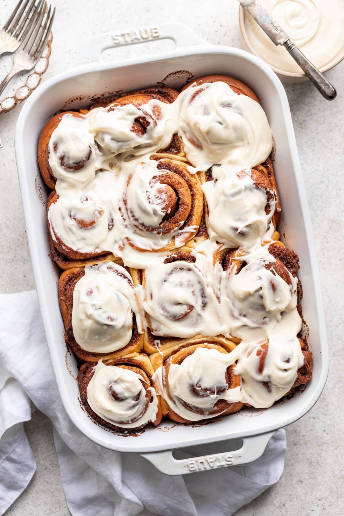 A white pan of baked overnight cinnamon rolls topped with cream cheese frosting.