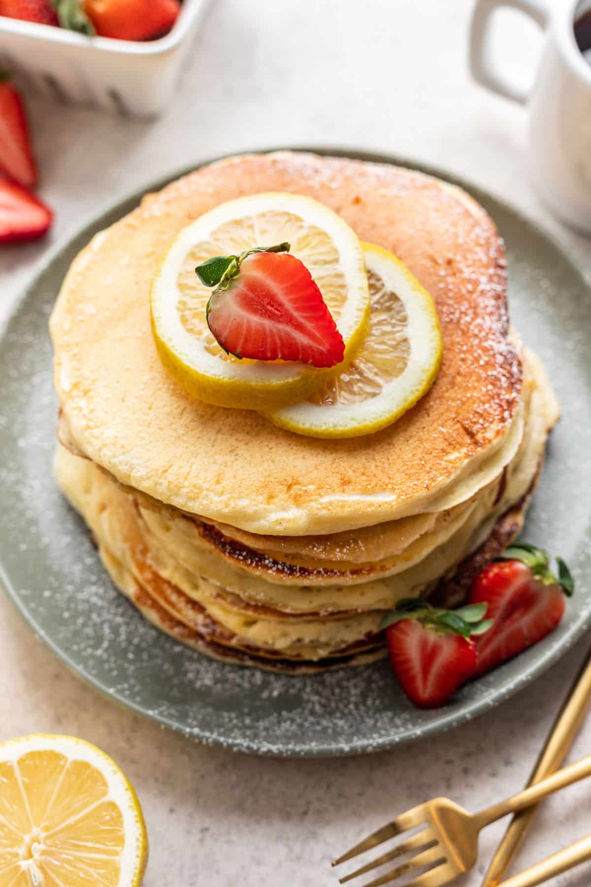 A stack of lemon ricotta pancakes next to a dish of strawberries. 