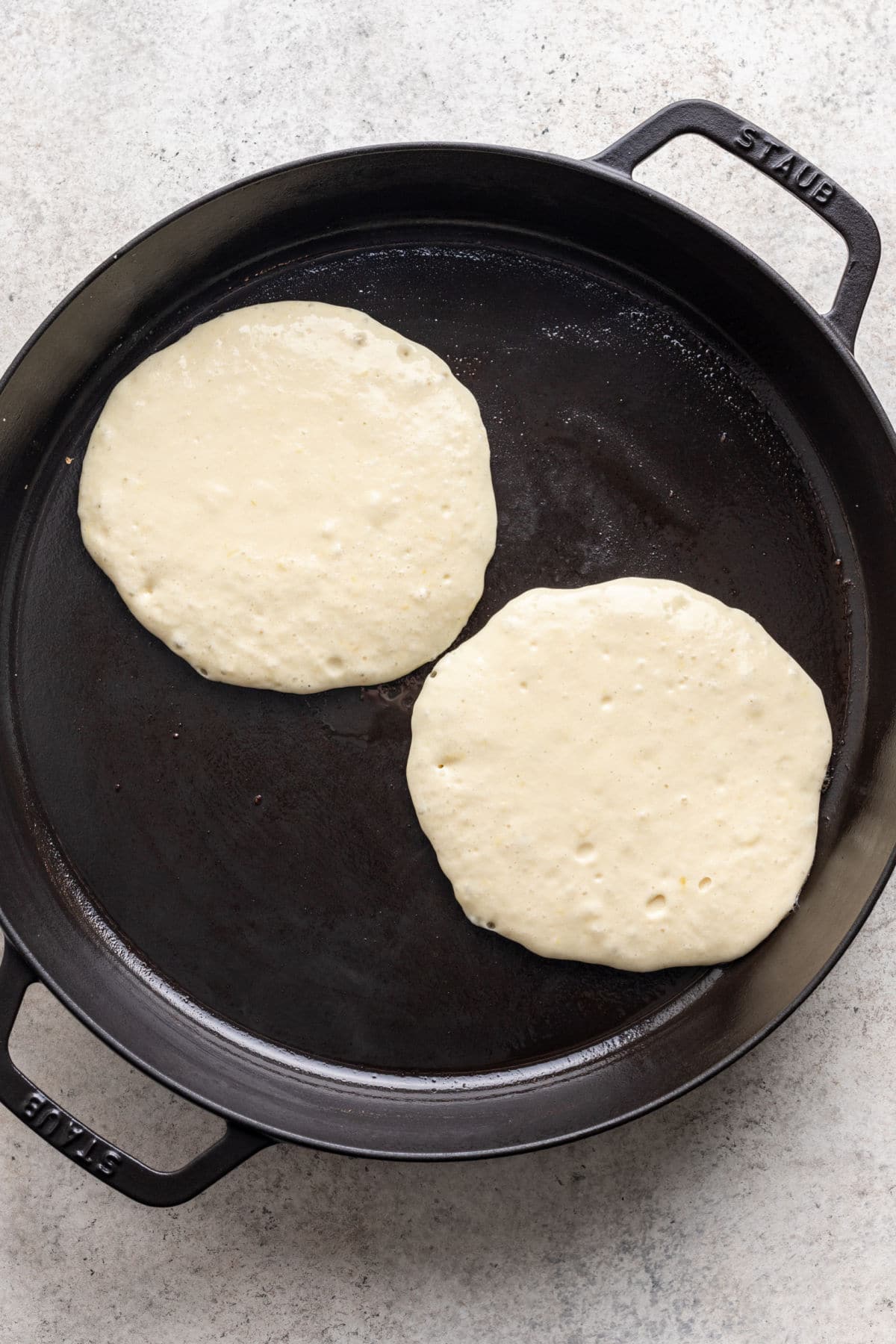 Two uncooked lemon ricotta pancakes in a skillet. 
