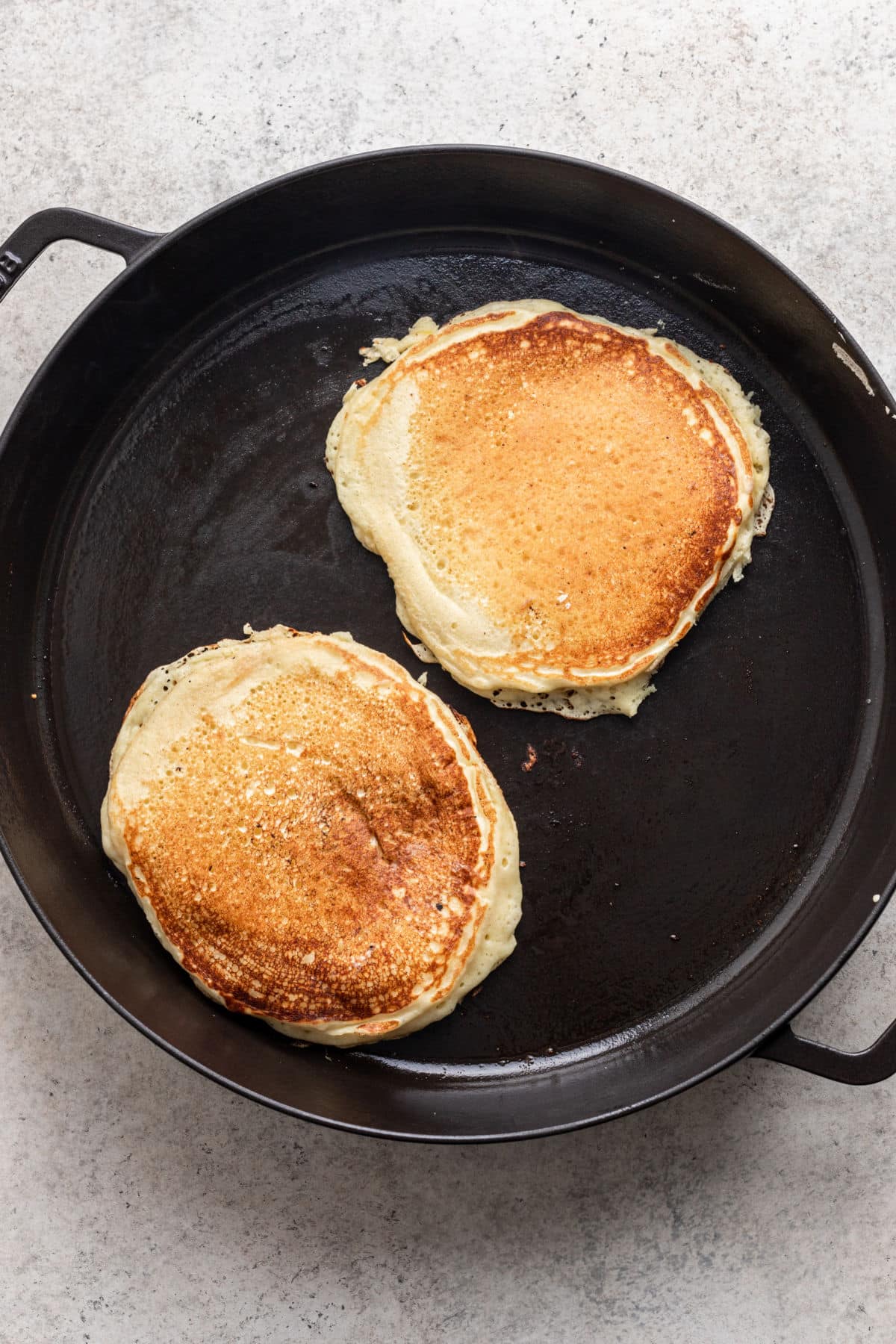 Two cooked lemon ricotta pancakes in a skillet. 