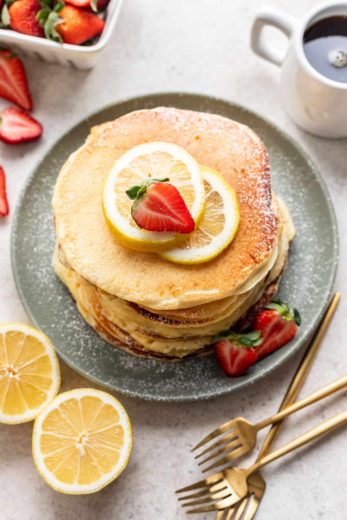 A plate of lemon ricotta pancakes next to three gold forks. 