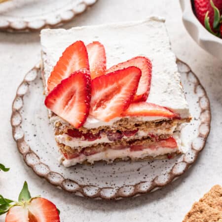 A slice of strawberry icebox cake next to a bowl of fresh strawberries.