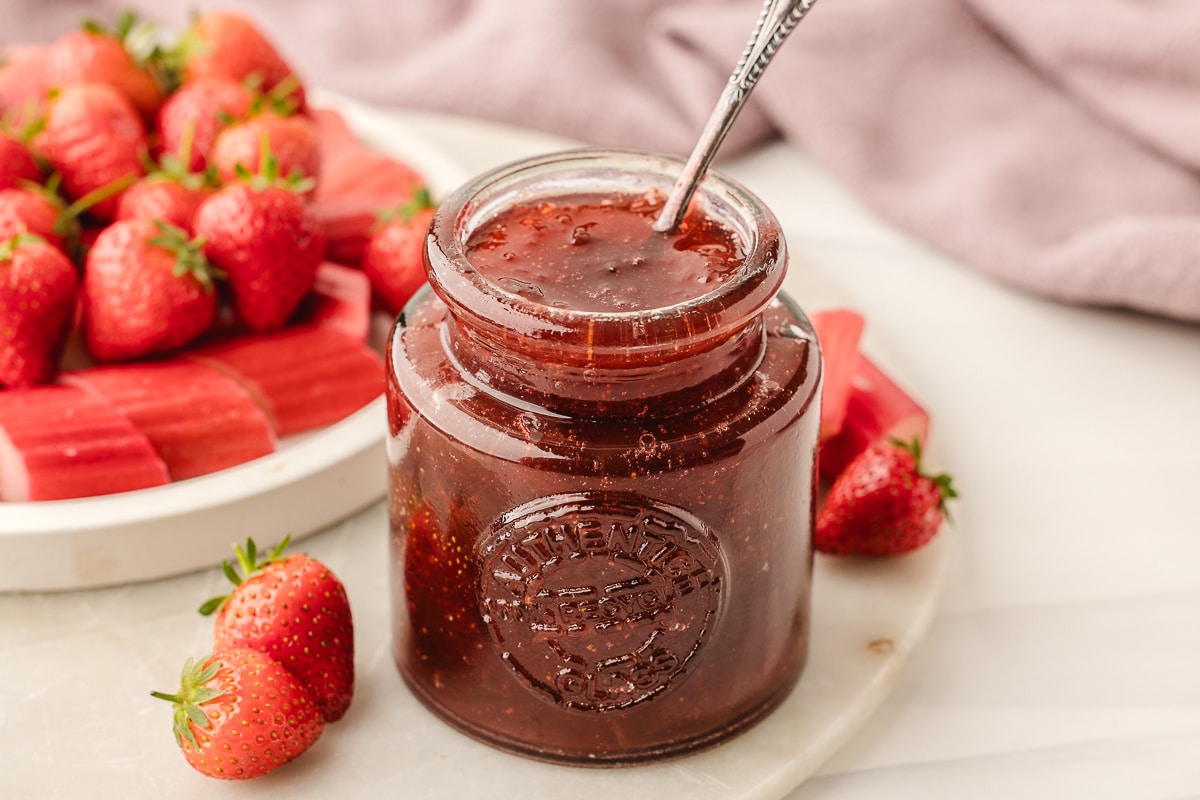 A jar of strawberry rhubarb jam next to fresh strawberries and cut rhubarb.