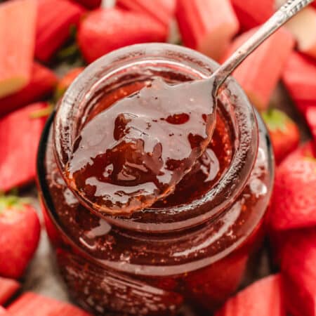 A silver spoon holding a scoop of strawberry rhubarb jam over the jar.