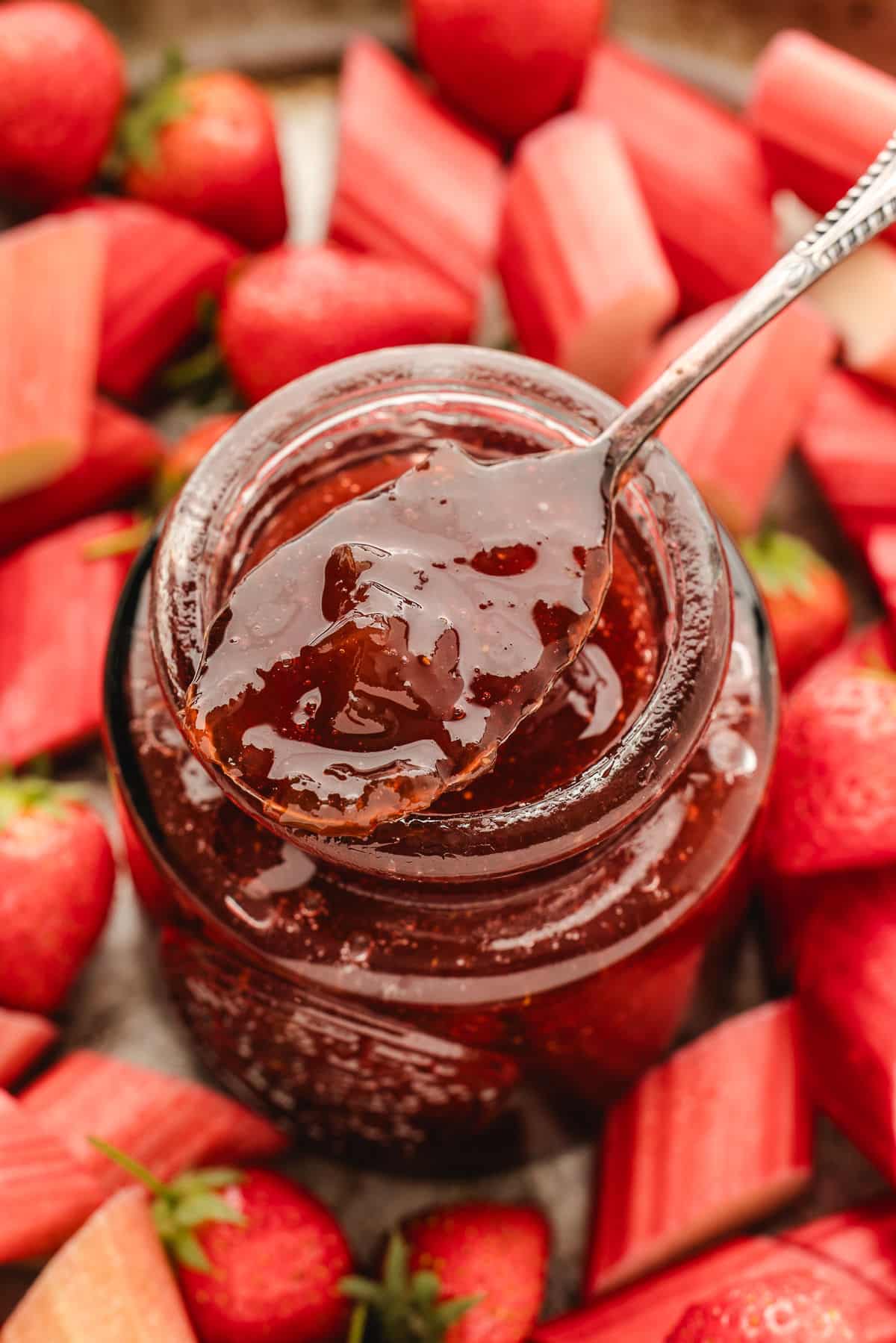 A silver spoon holding a scoop of strawberry rhubarb jam over the jar. 