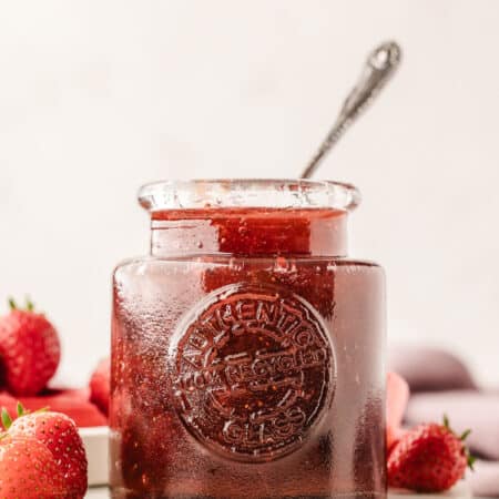 A glass jar full of strawberry rhubarb jam with a silver spoon in it.