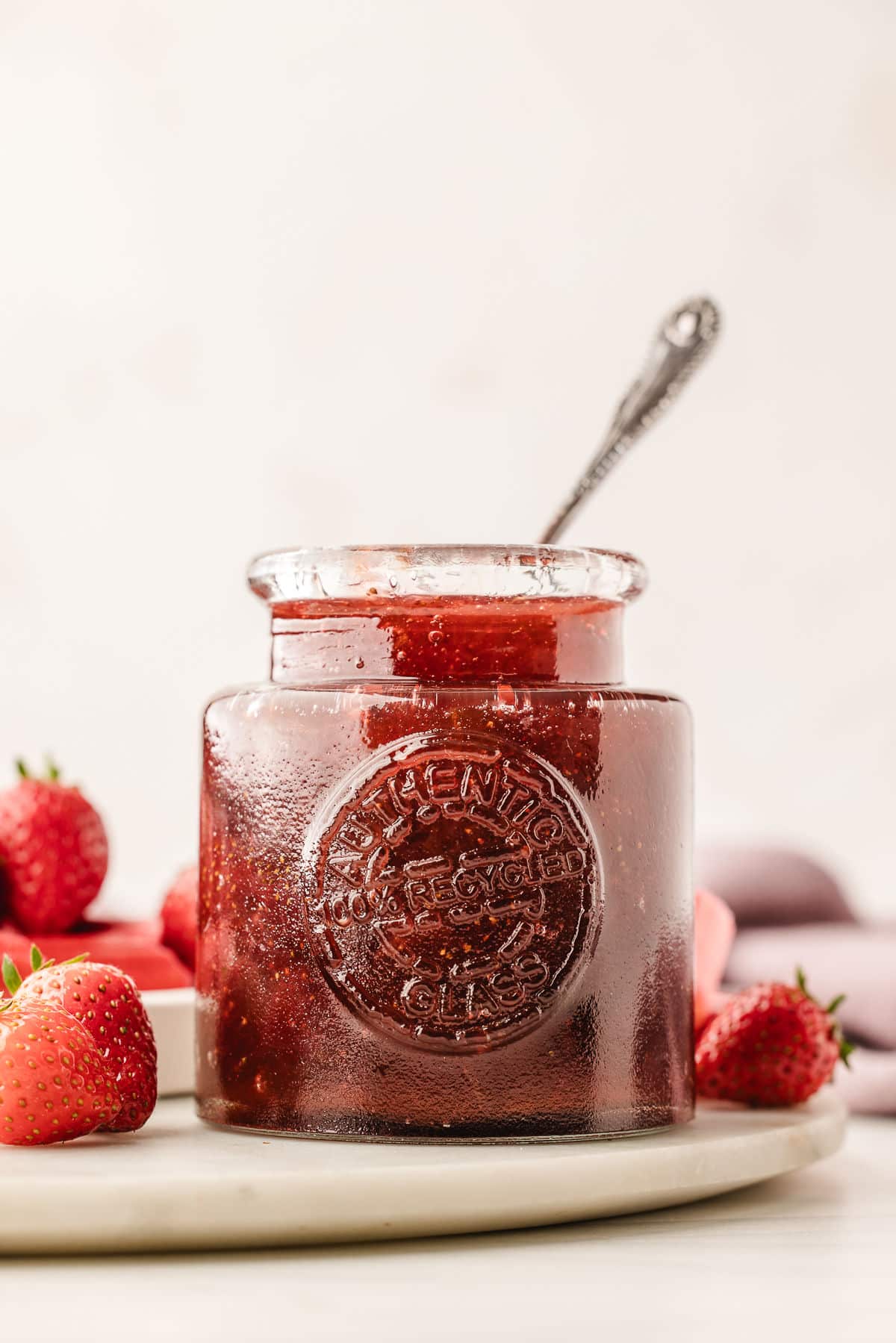 A glass jar full of strawberry rhubarb jam with a silver spoon in it.