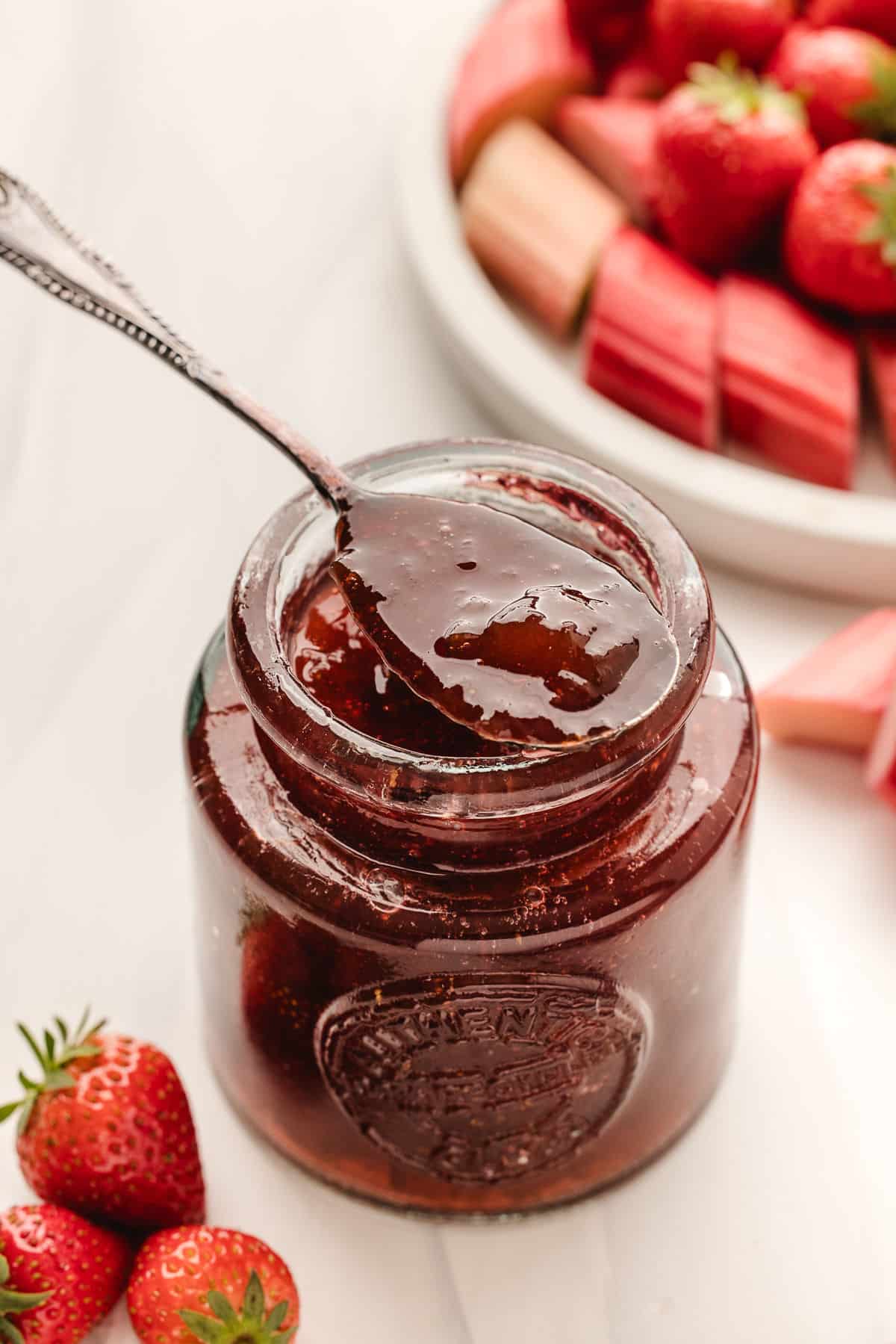 A spoonful of strawberry rhubarb jam resting on the edge of the jar. 