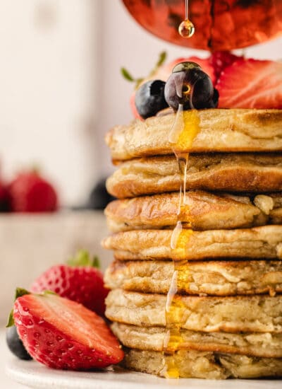 Maple syrup pouring onto a stack of sweet cream pancakes.