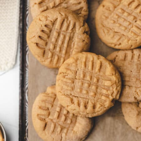 Overlapping peanut butter cookies on a piece of brown parchment paper.