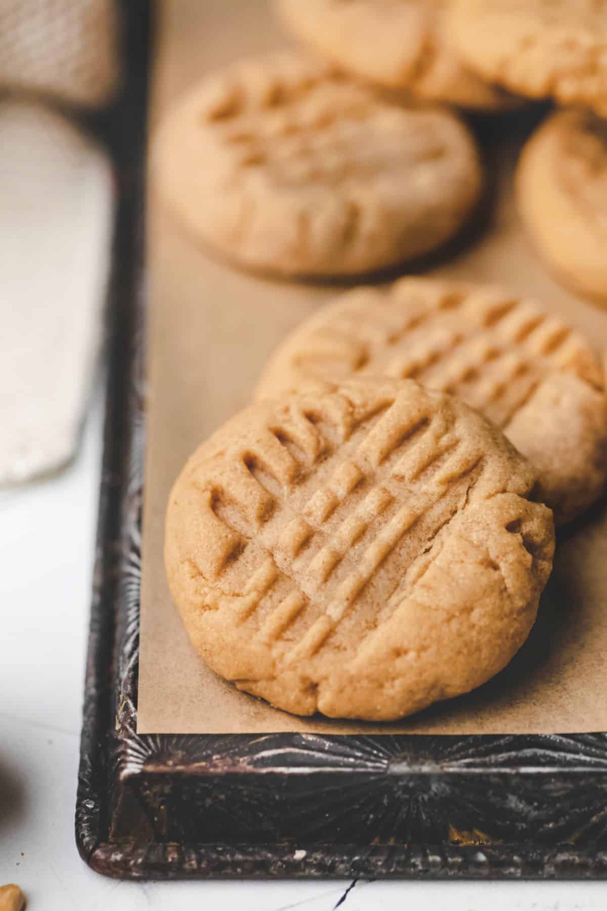 A peanut butter cookie leaning on other cookies on a piece of brown parchment paper. 