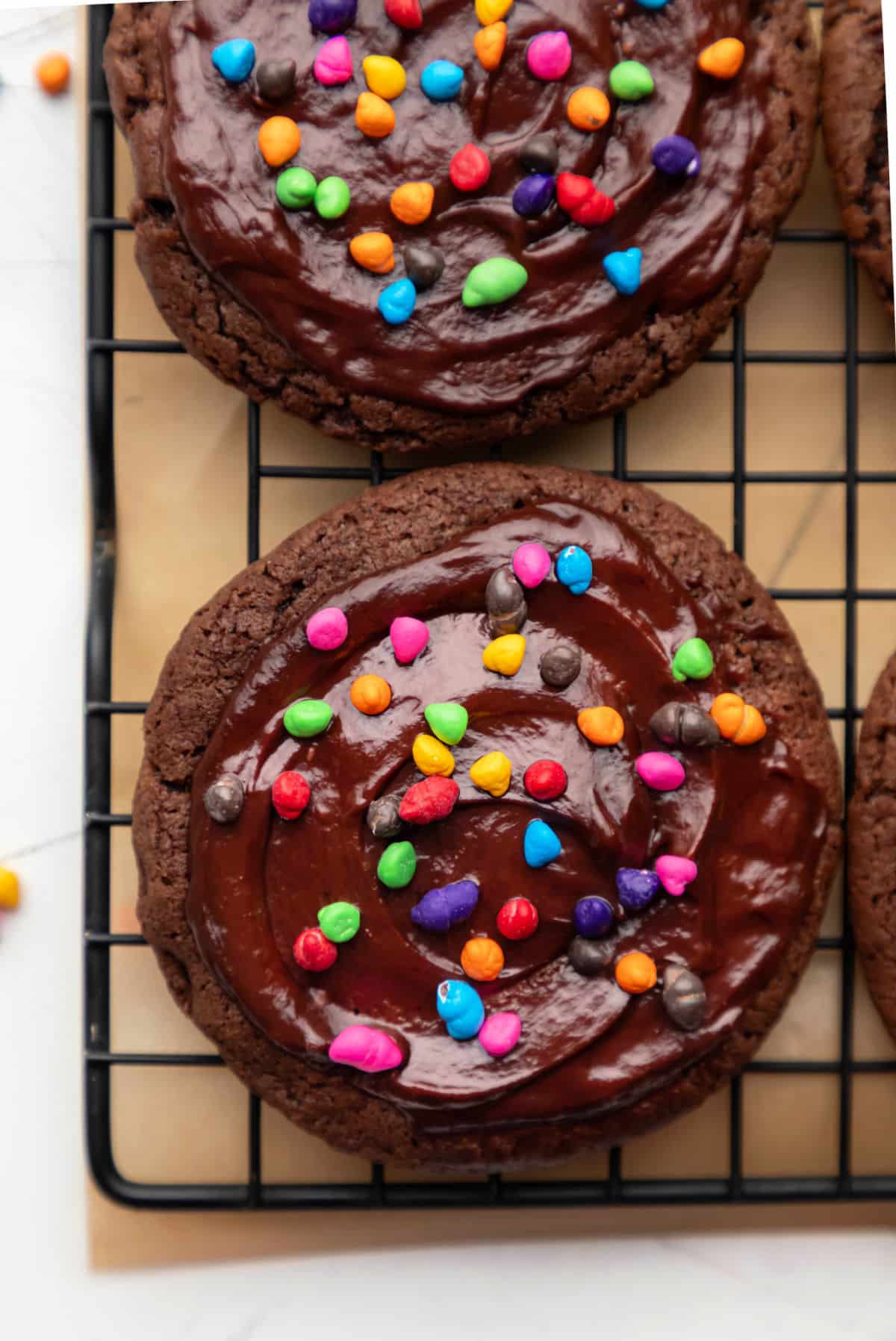 Two cosmic brownie cookies on a wire cooling rack over a piece of brown parchment paper.