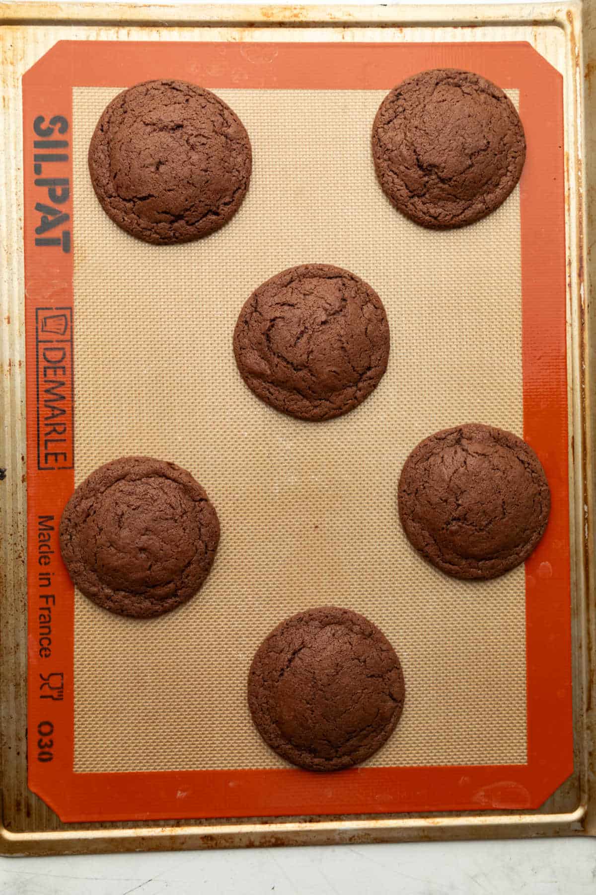 Six baked cosmic brownie cookies on a baking sheet. 