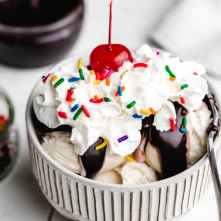 Homemade hot fudge on scoops of vanilla ice cream with whipped cream and a cherry on top.