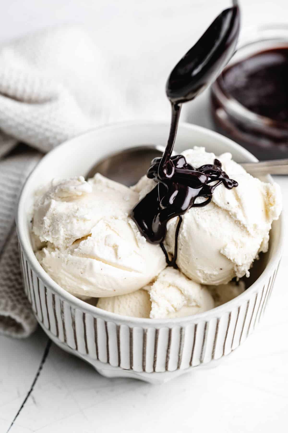 A spoon drizzling hot fudge over scoops of vanilla ice cream. 
