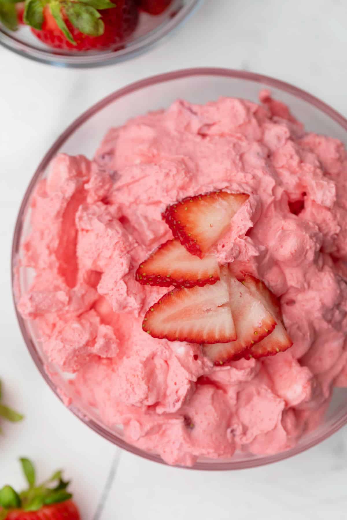 A glass bowl of strawberry fluff next to a dish of fresh strawberries.  