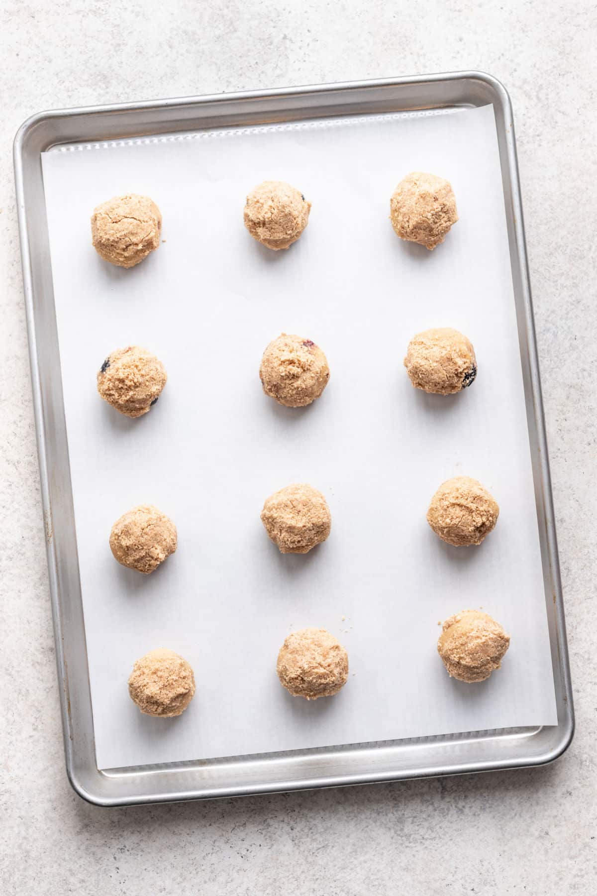 Scoops of blueberry muffin cookie dough on a cookie sheet. 