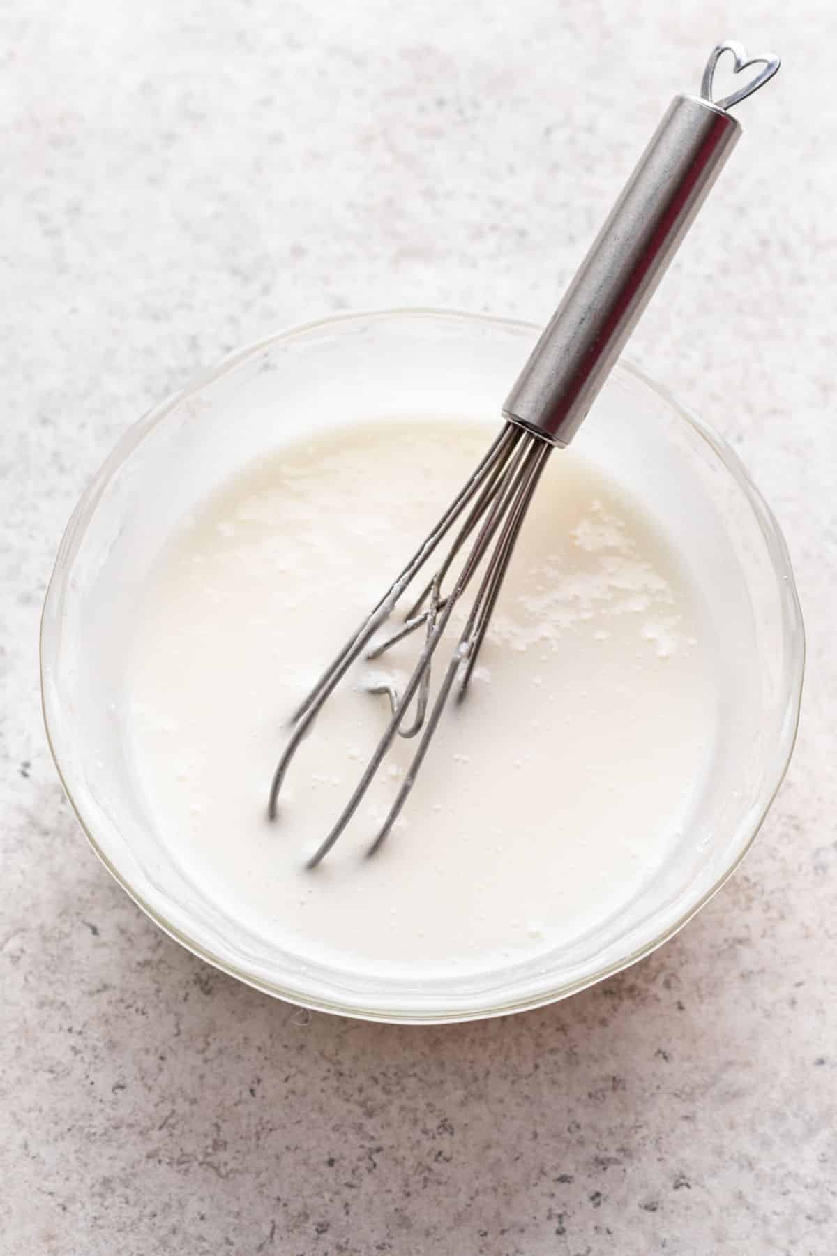 Glaze in a white mixing bowl with a whisk in it. 