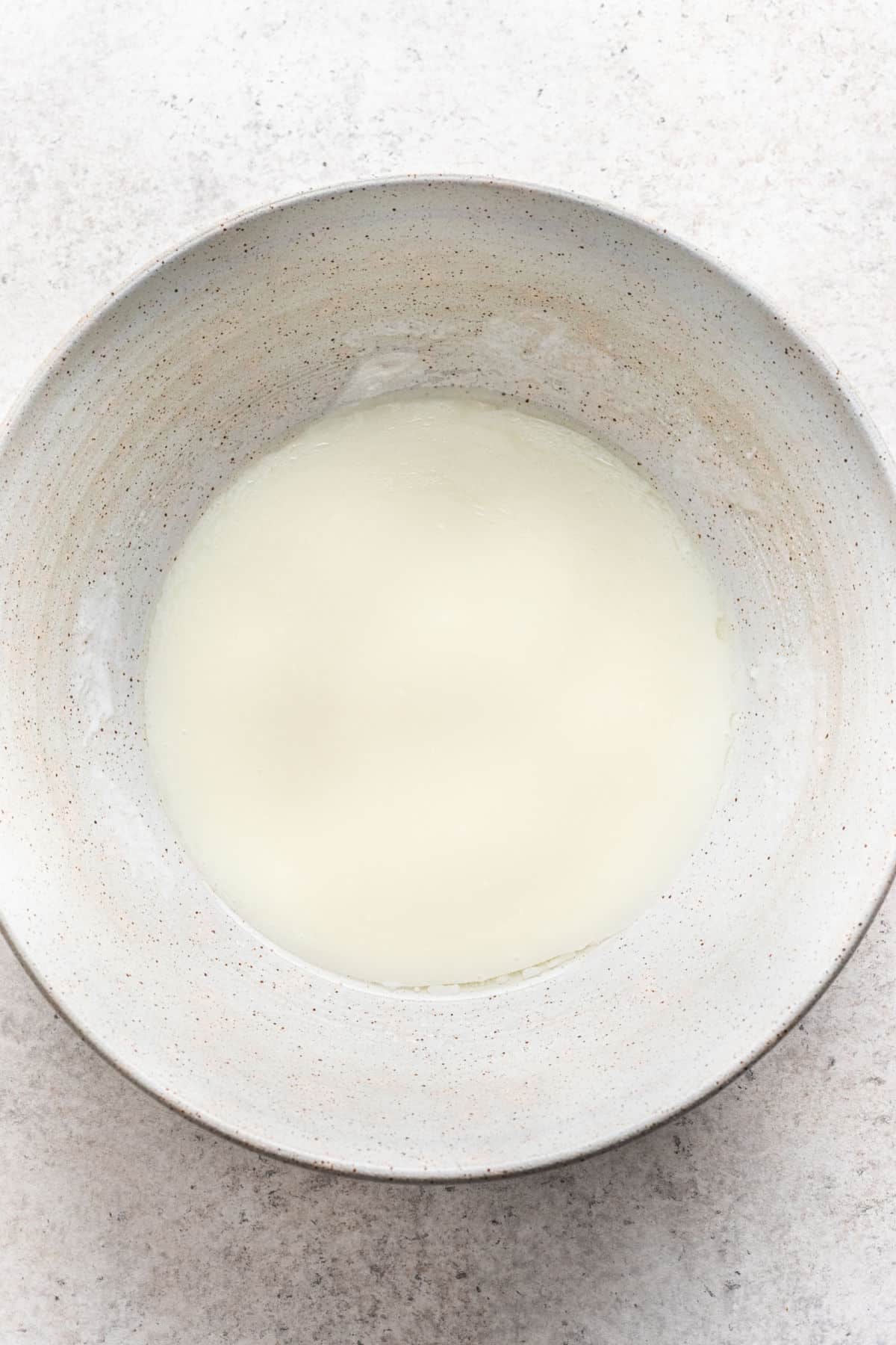 Oil, buttermilk, sour cream, and sugar mixed together in a white mixing bowl. 