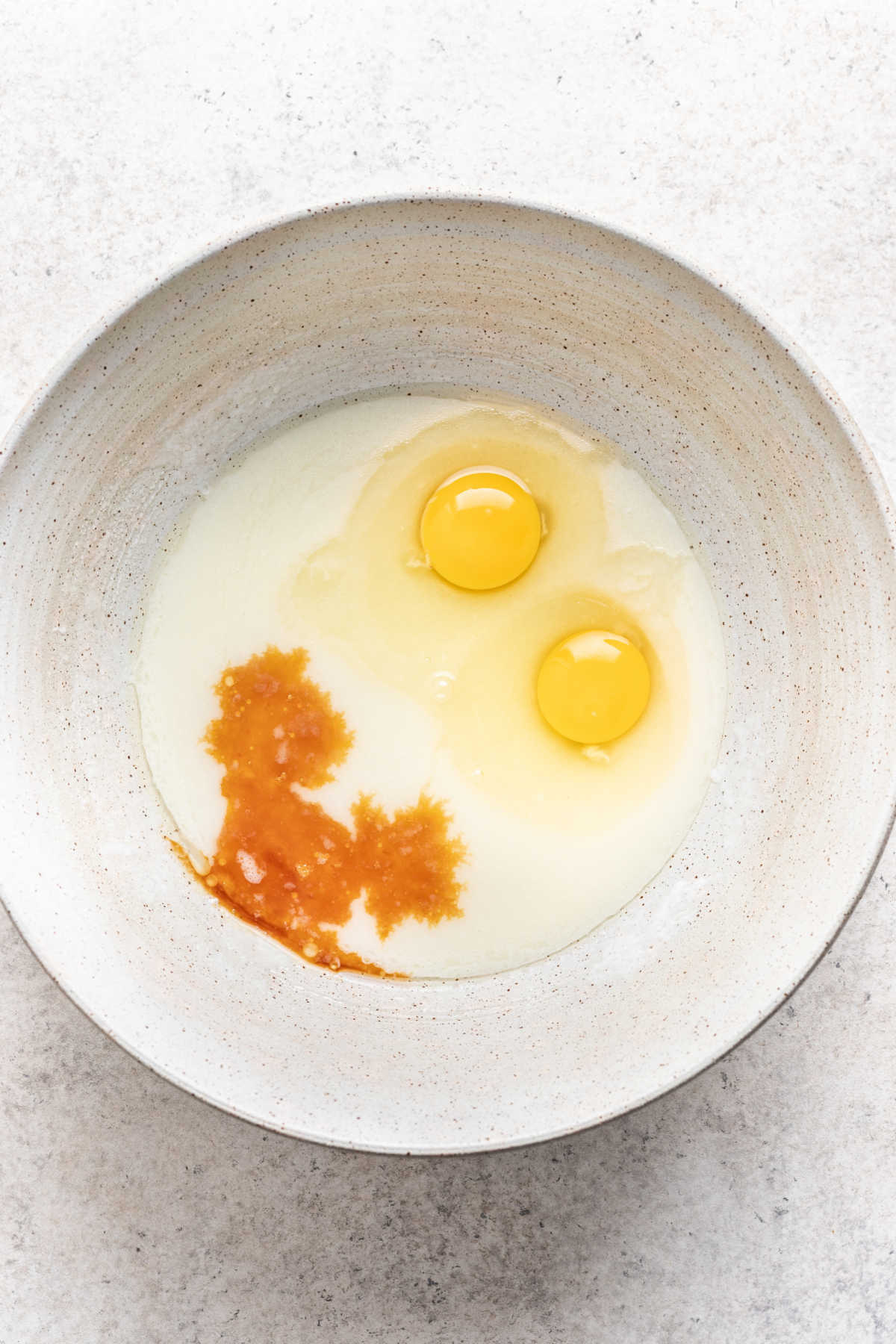 Eggs and vanilla on top of wet ingredients in a white mixing bowl. 