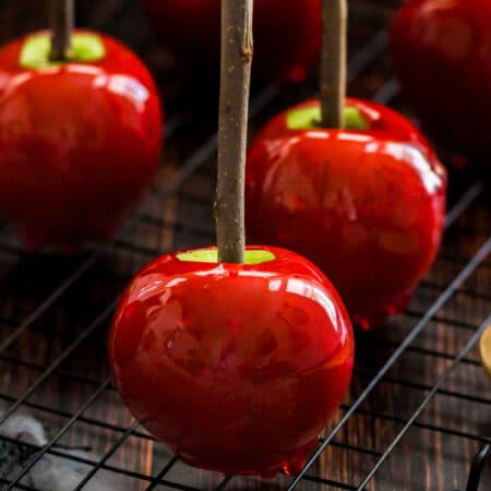 Candy apples with a wooden stick stem on a black wire cooling rack.