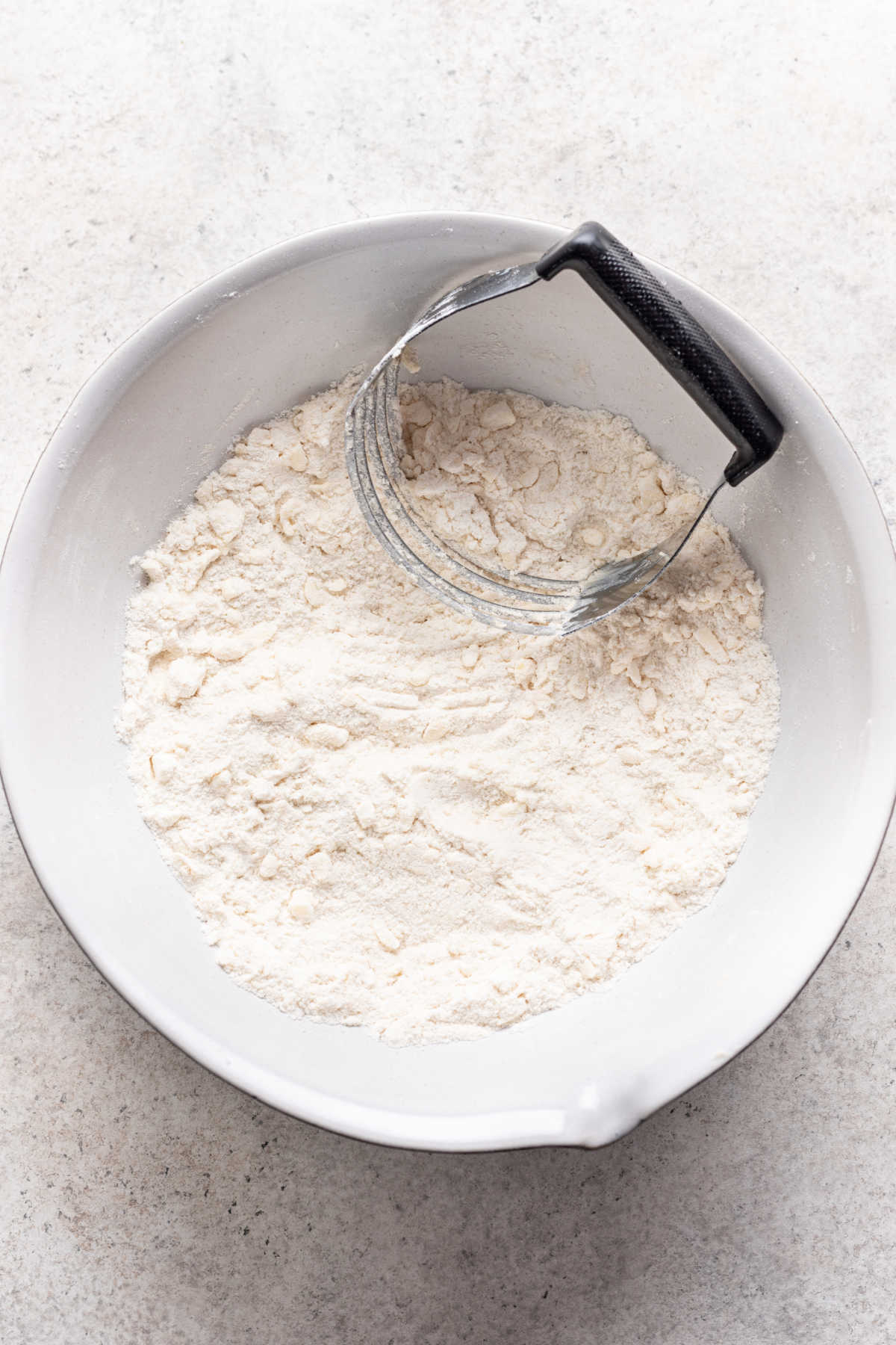 A pastry cutter cutting butter into dry ingredients for strawberry scones. 