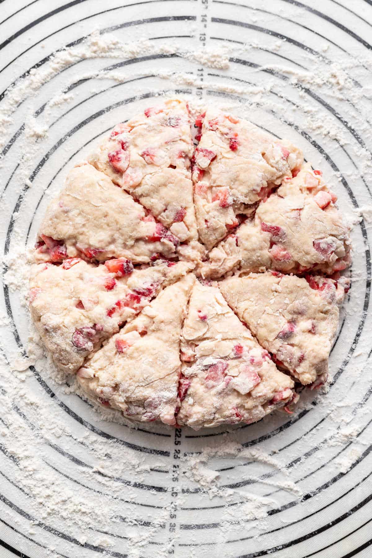 Round patted strawberry scone dough cut into triangles. 