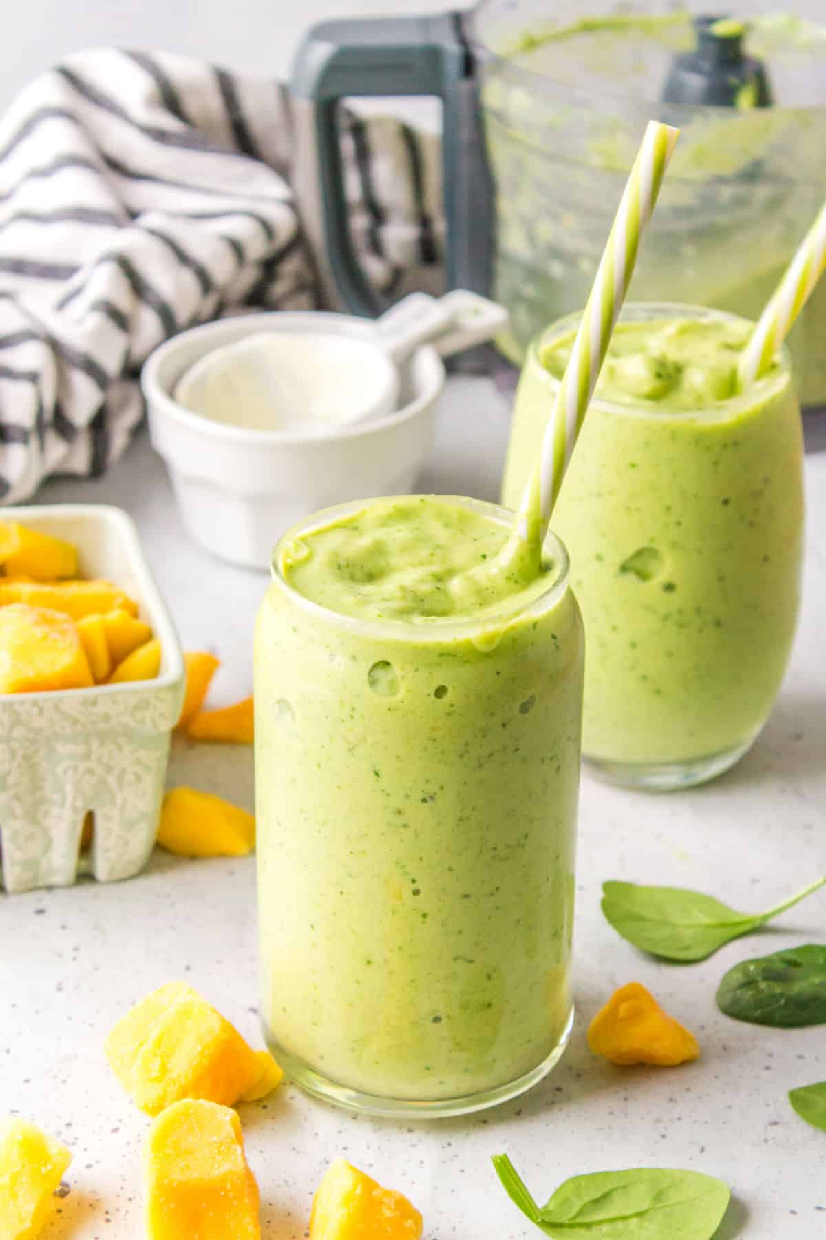 Two glasses of green smoothie with straws in them. 