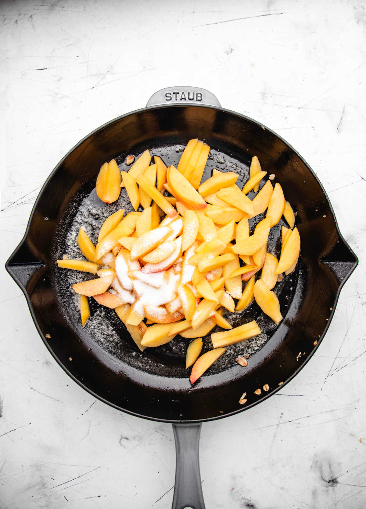 Peach slices and sugar in a gray skillet. 