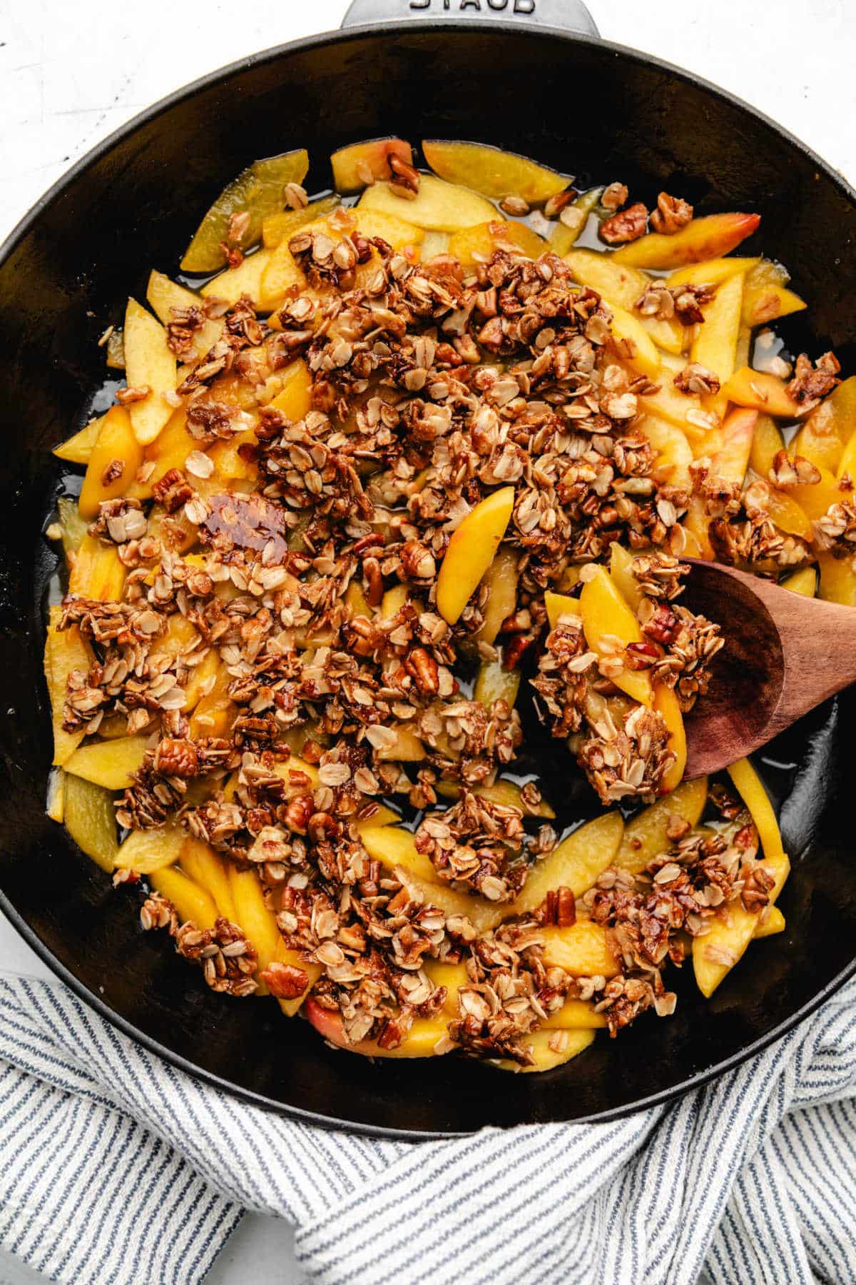 A skillet of easy peach crisp with a wooden spoon in it. 