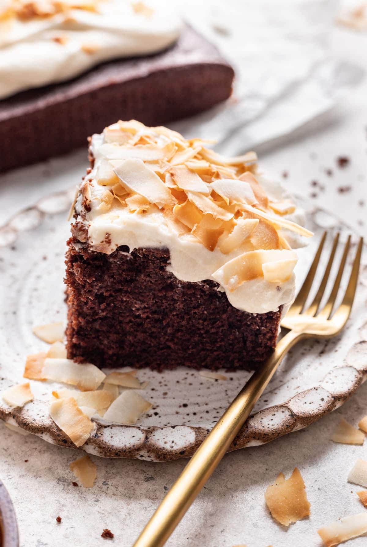 A piece of chocolate coconut cake on a plate with a gold fork next to it.