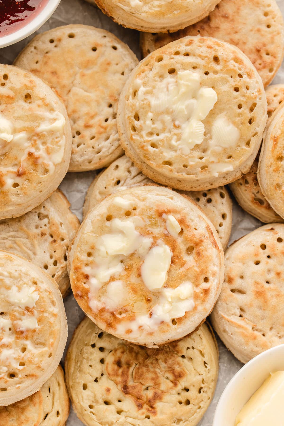 Overlapping English crumpets with butter on some of the crumpets.