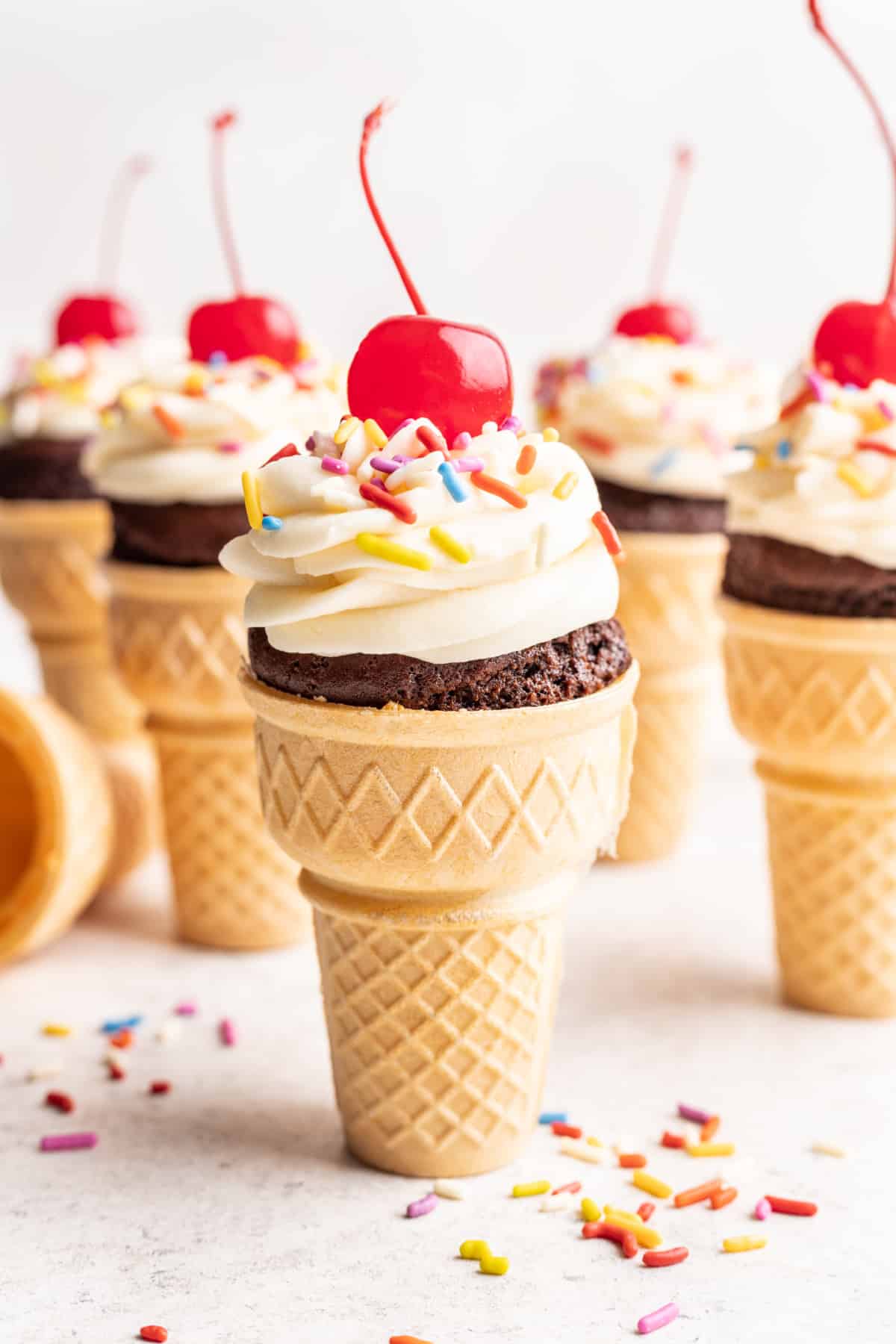 Ice cream cone cupcakes topped with vanilla frosting sprinkles and a cherry.