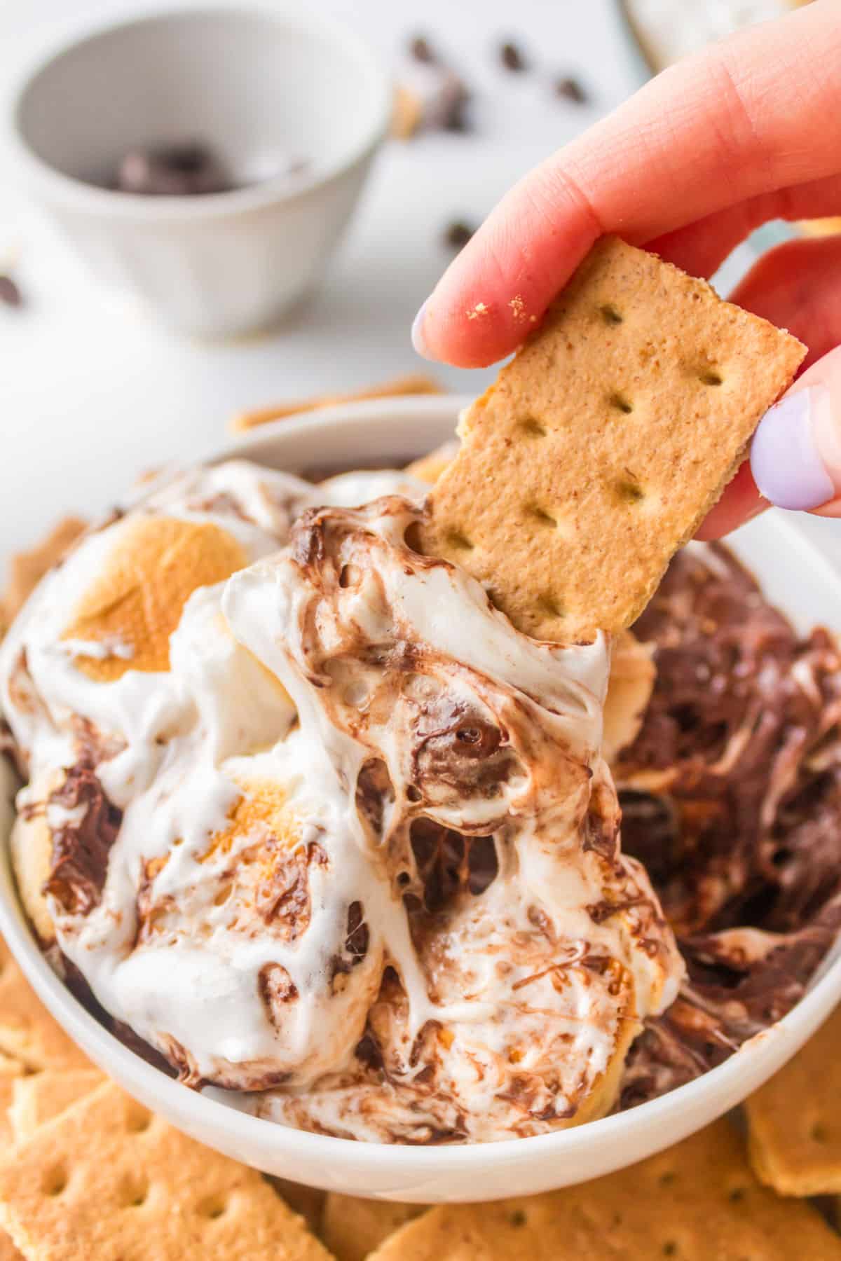 A graham cracker dipping s'mores dip in a white bowl. 