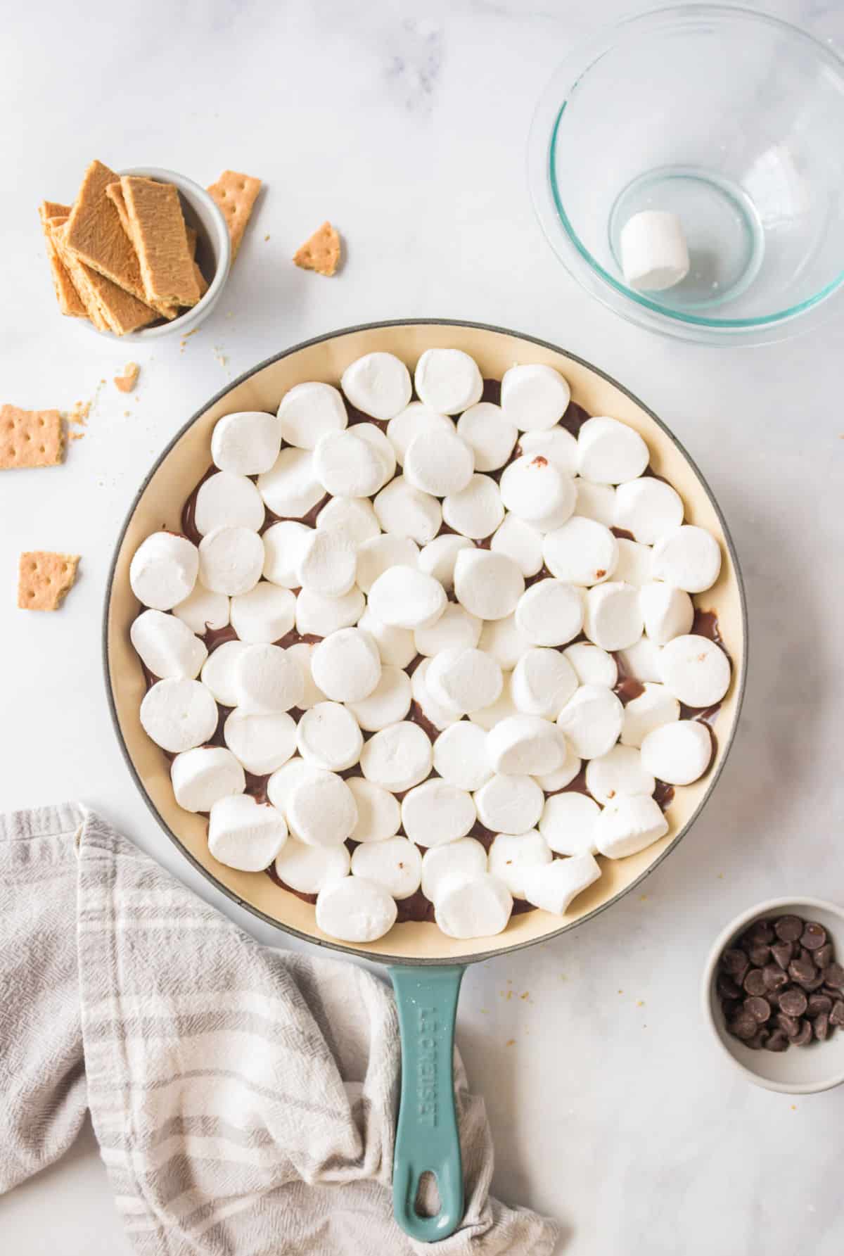 Marshmallows on top of chocolate chips in a cast iron skillet. 