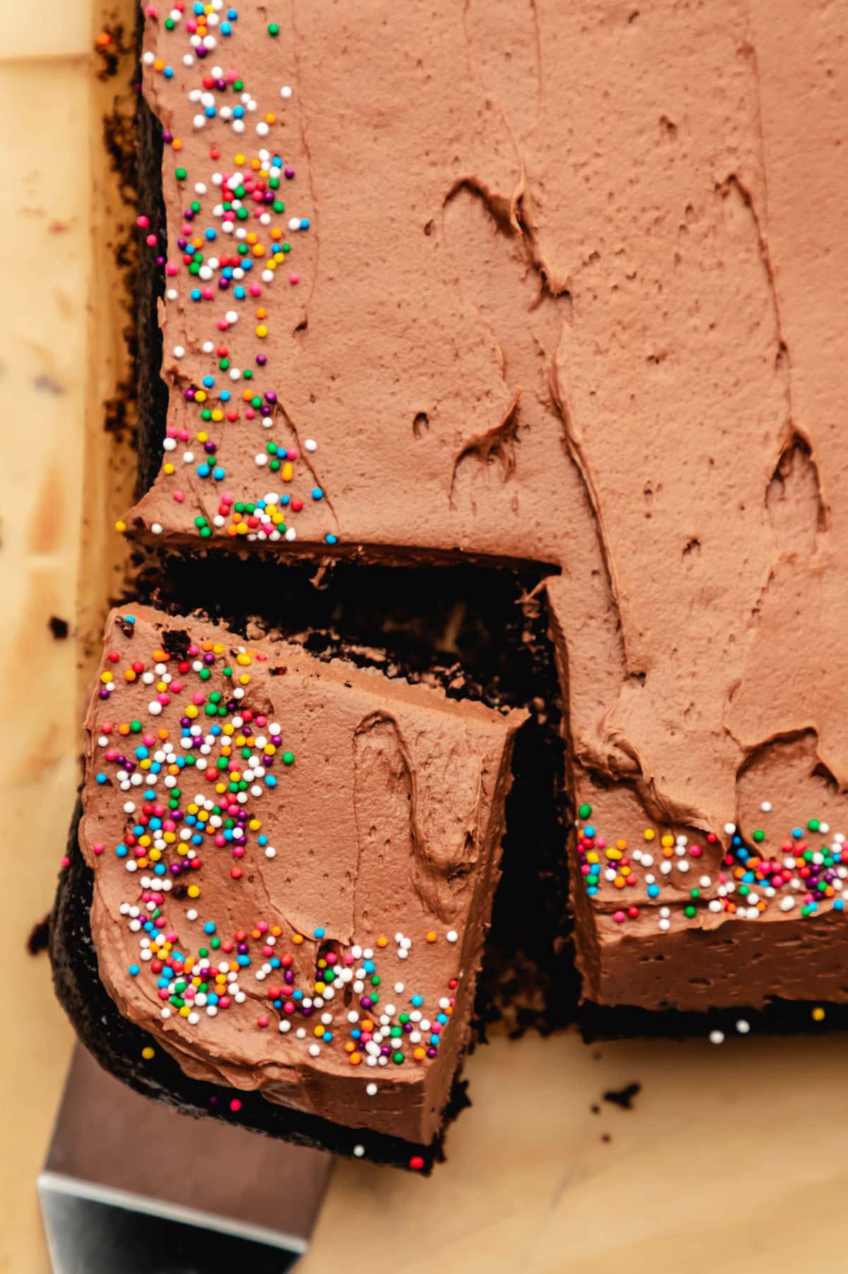 A slice of chocolate sheet cake at an angle next to the cake. 