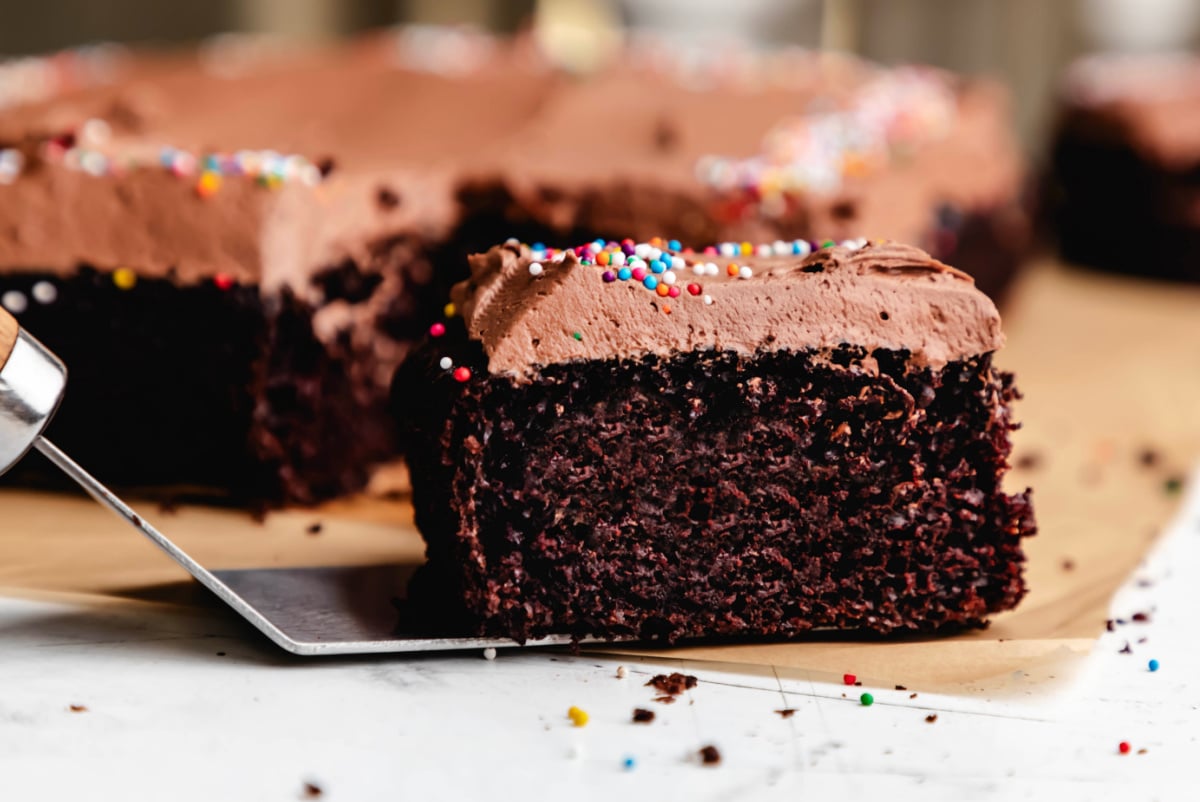 A slice of chocolate sheet cake frosted with chocolate frosting and non pareils. 