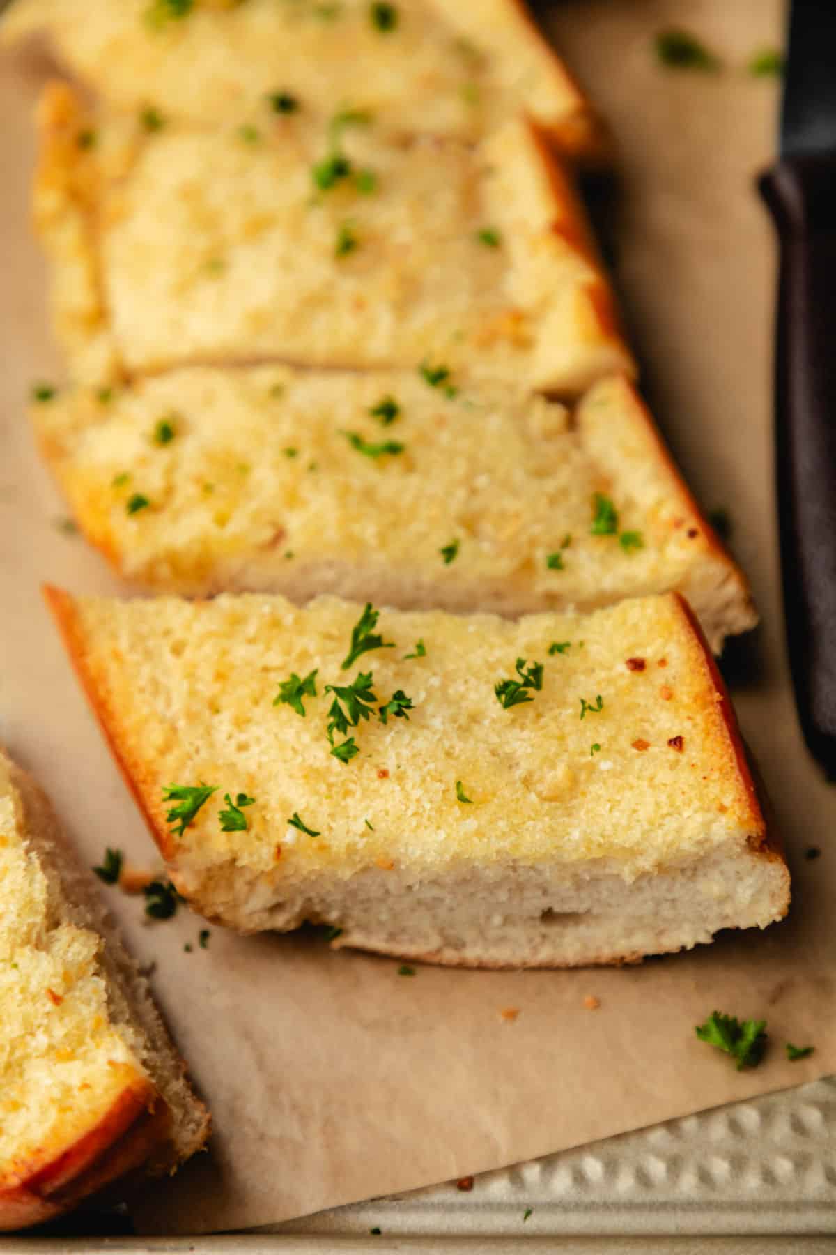 Sliced homemade garlic bread on brown parchment paper.