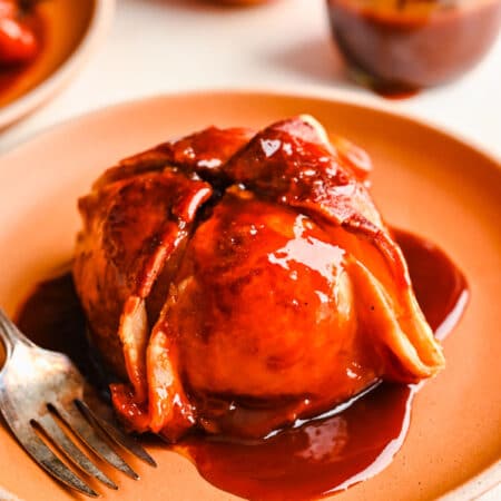 A pastry wrapped apple dumpling on an orange plate.