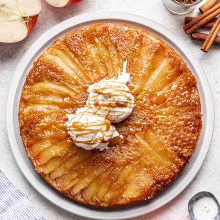 An apple upside down cake next to apples and cinnamon sticks.