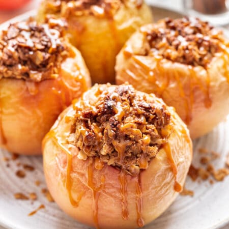 Baked apples drizzled with caramel on a white plate.