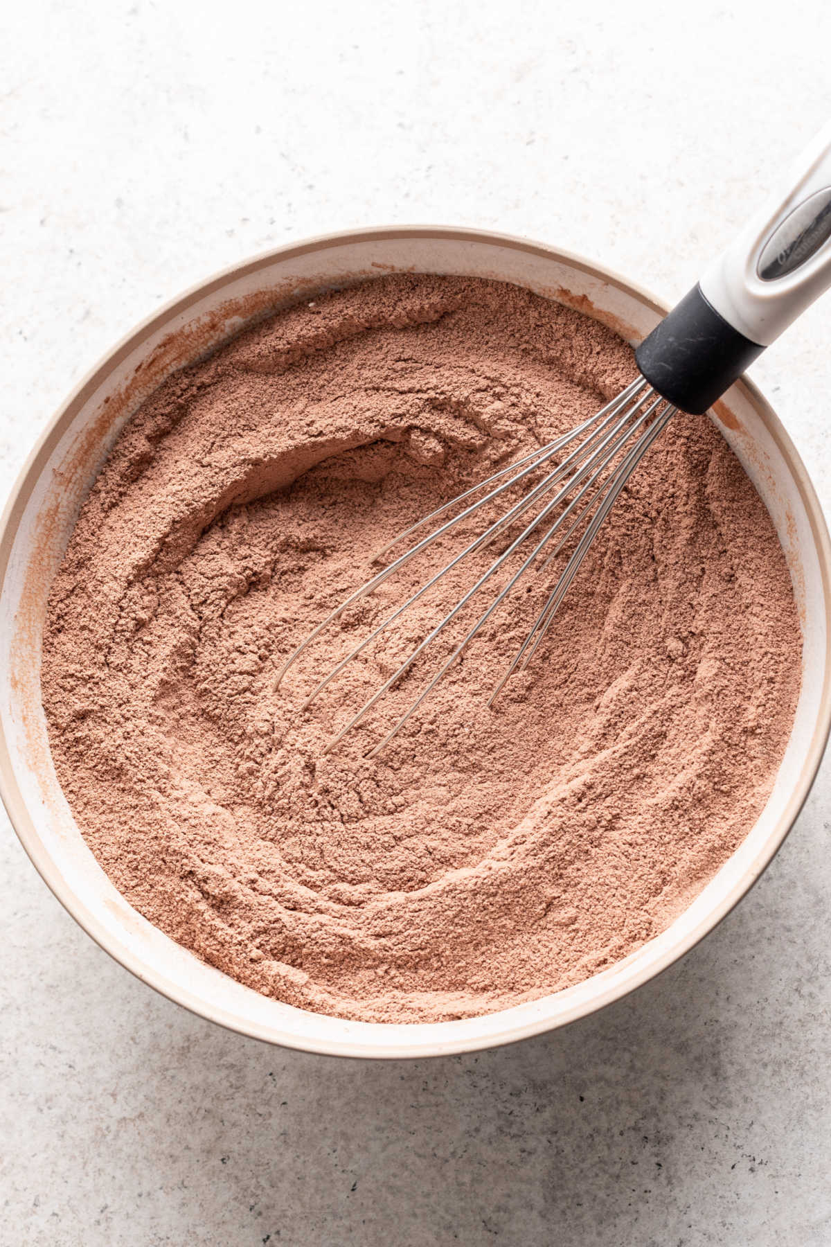 A whisk whisking dry ingredients for chocolate mousse cake in a bowl. 