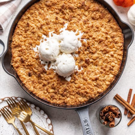 A cast iron skillet filled with pumpkin crisp and topped with three scoops of vanilla ice cream.