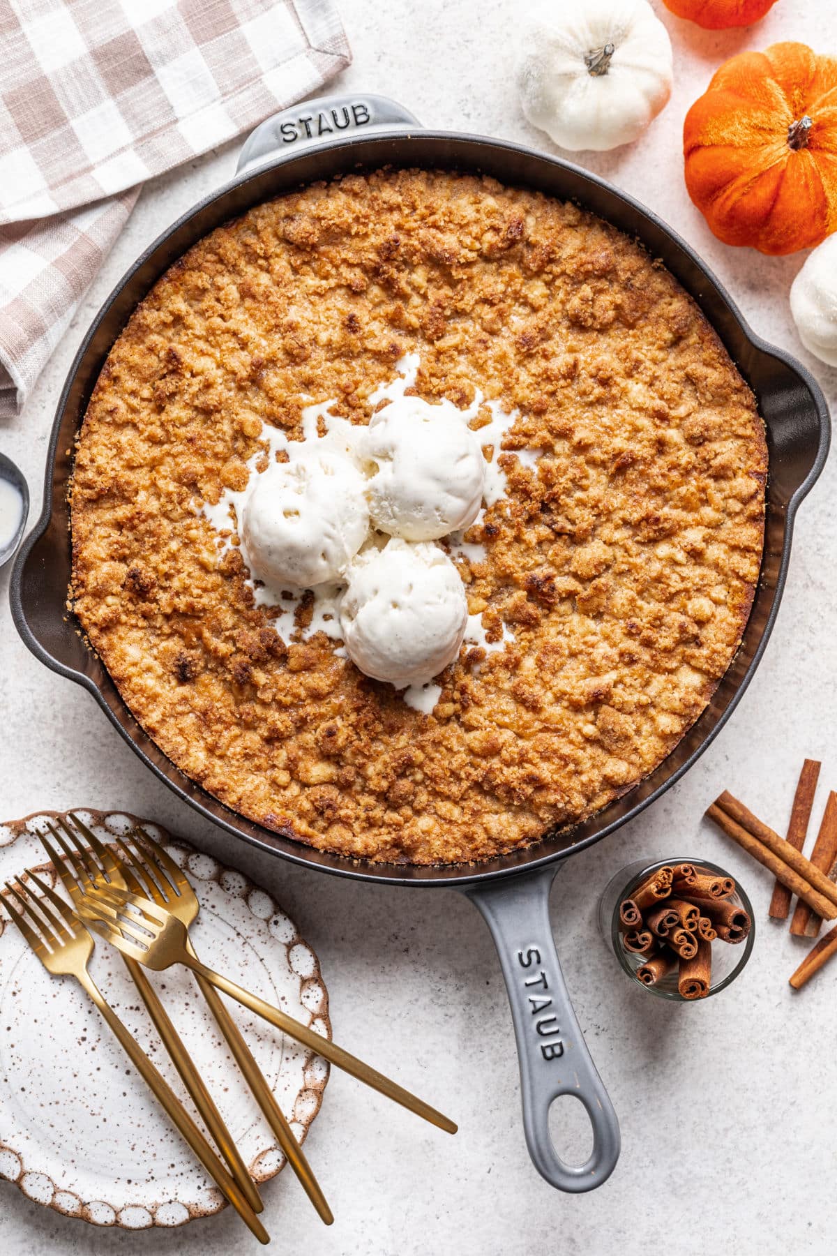 A cast iron skillet filled with pumpkin crisp and topped with three scoops of vanilla ice cream.